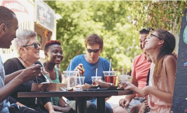 Group of people eating and drinking around a table outside, laughing