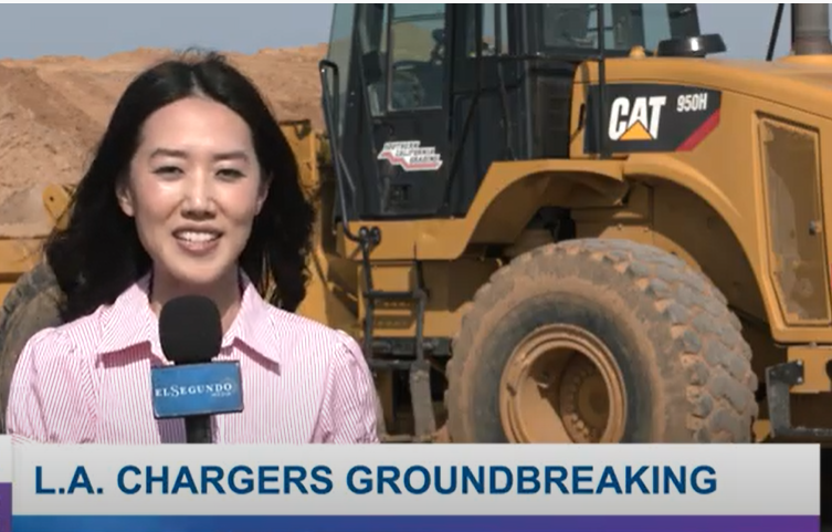 Reporter with microphone in front of bulldozer and dirt at Chargers Groundbreaking