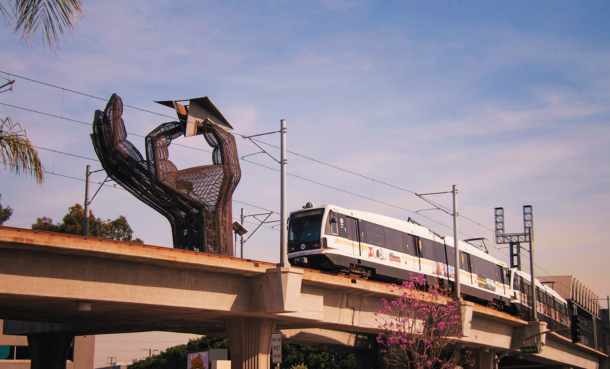 Train on rails at El Segundo Metro Station in front of hand and airplane sculpture