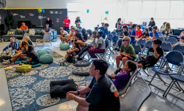 Kids sitting on floor and chairs at teen center watching Little League World Series